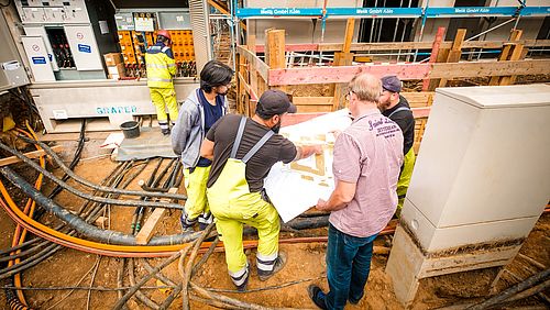 Mehrere Mitarbeitende in Sicherheitskleidung zeigen Kunden einen Anschlussplan auf einer Baustelle