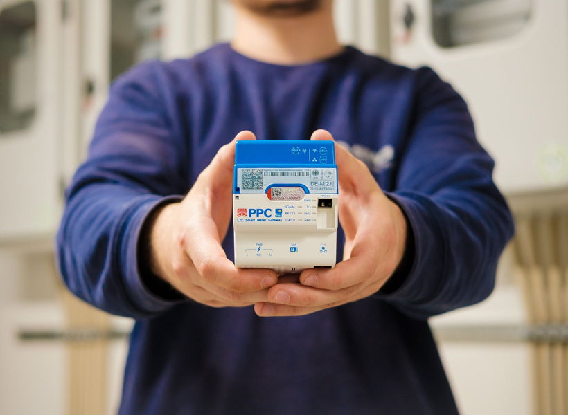Ein Mann mit einem blauen Pulli hält ein Smart-Meter-Messgerät in den Händen. Er streckt es nach vorne in die Kamera, der Hintergrund ist unscharf.